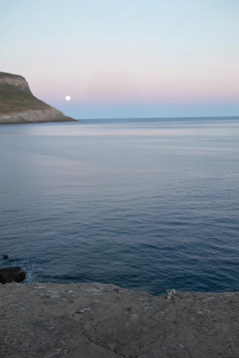 Calm ocean water with distant cliffs and moonrise