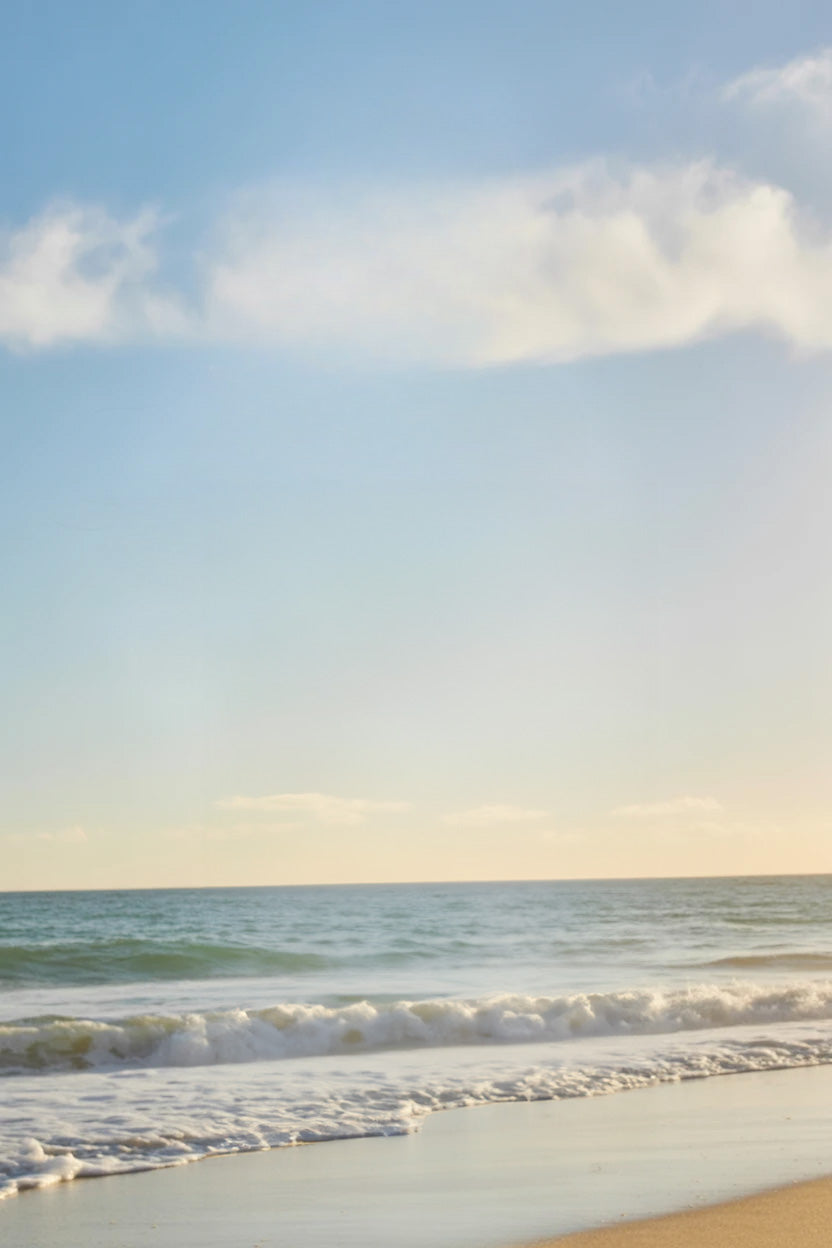 Sunny beach shoreline with gentle ocean waves and clouds