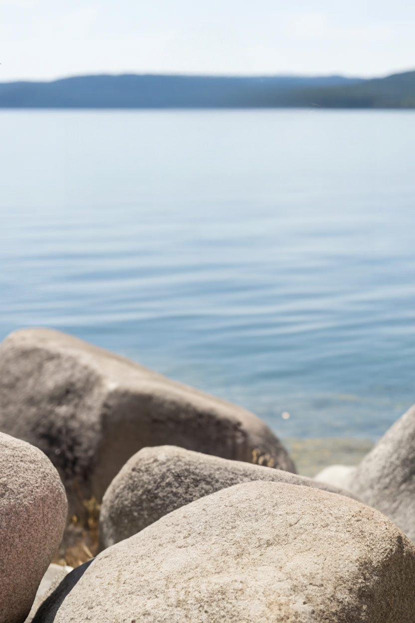 Calm lake with distant hills and large shoreline rocks