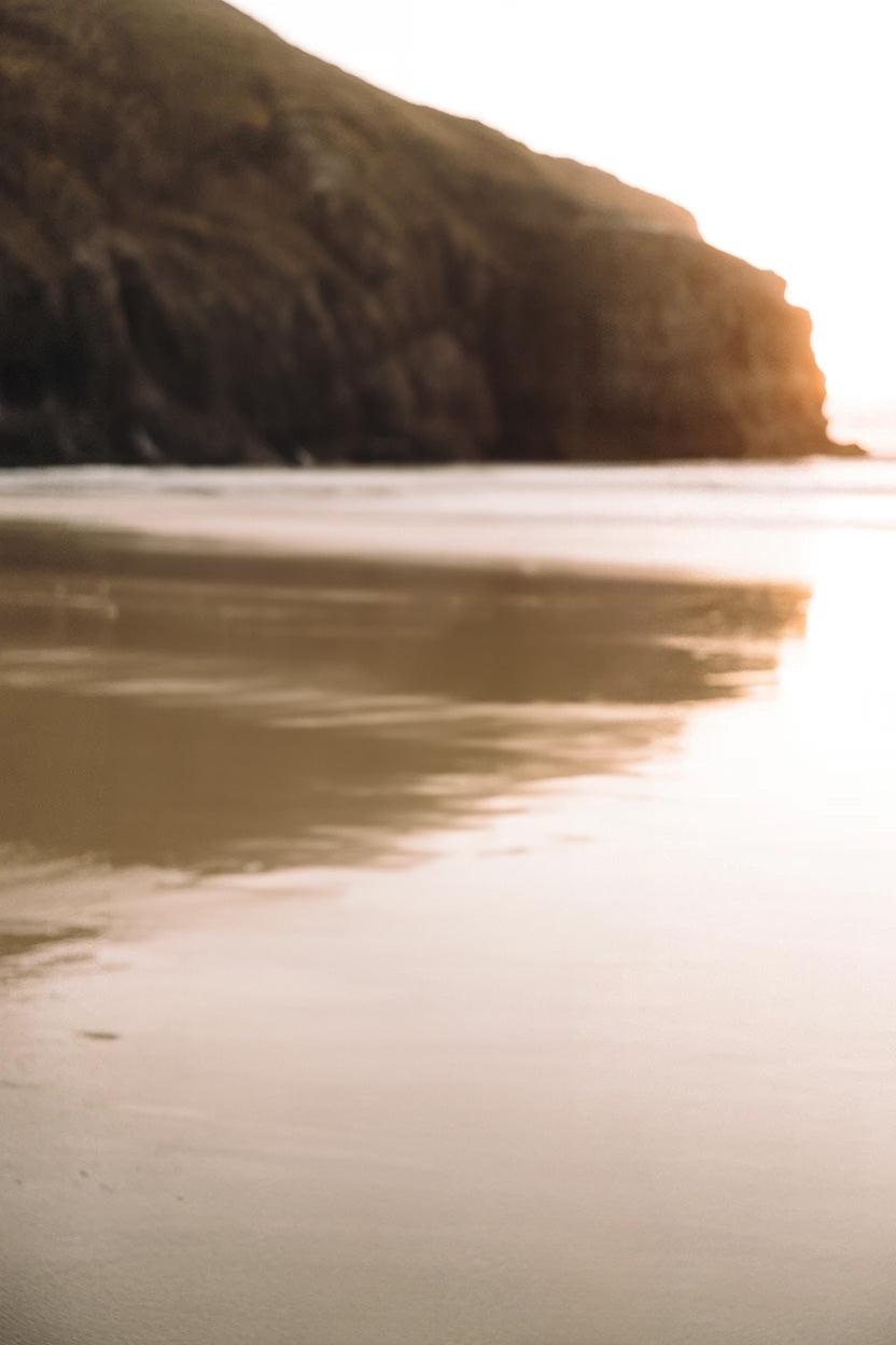 Golden beach shoreline with rocky cliff at sunset glow