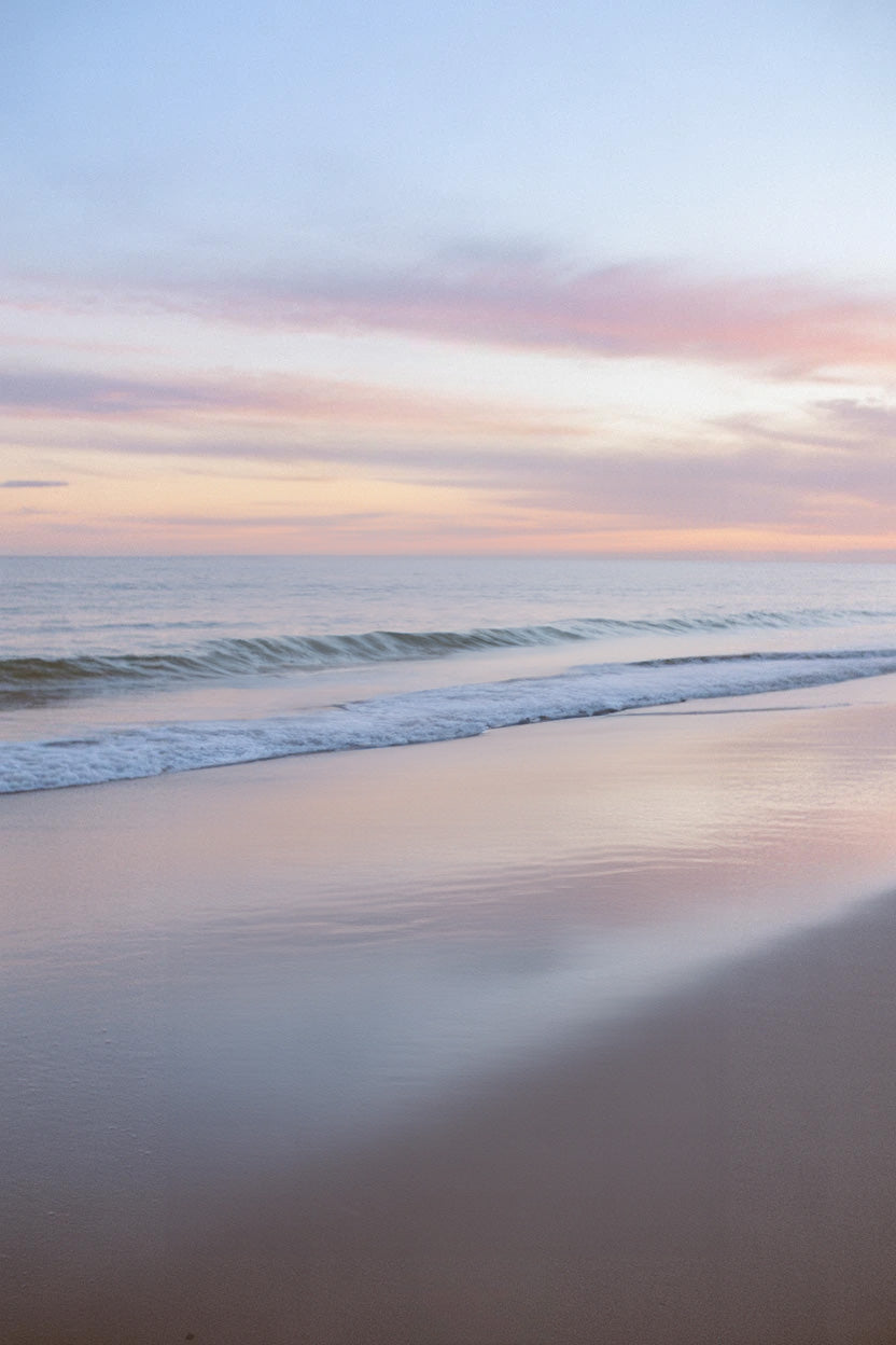Calm ocean shoreline with pastel sunset sky reflections