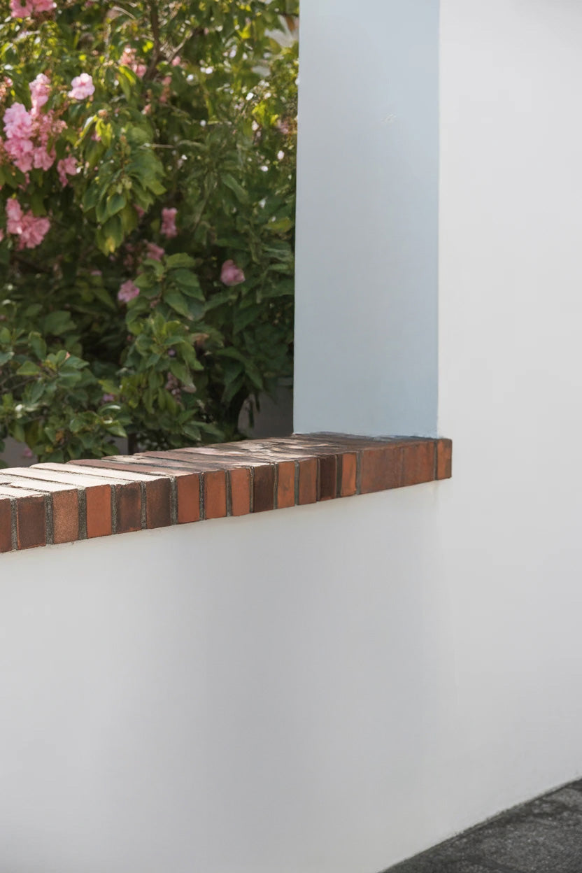 White wall with brick trim and blooming pink flowers behind