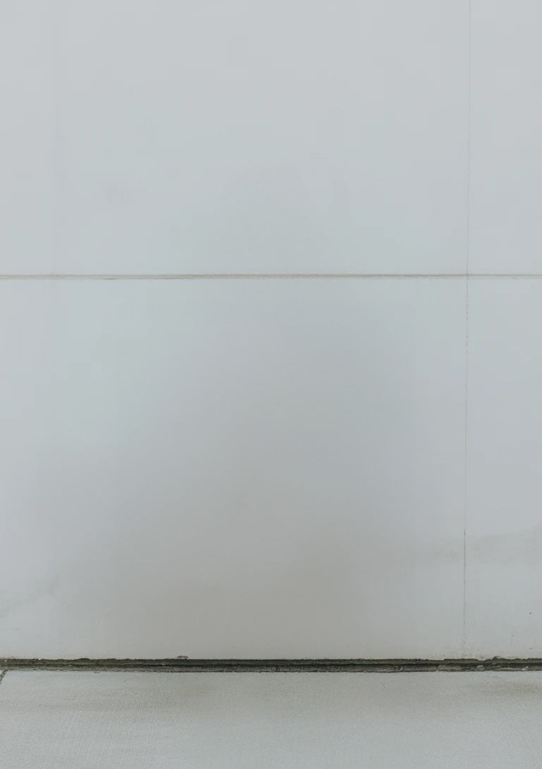 Minimalist white tiled wall with subtle shadow and concrete floor