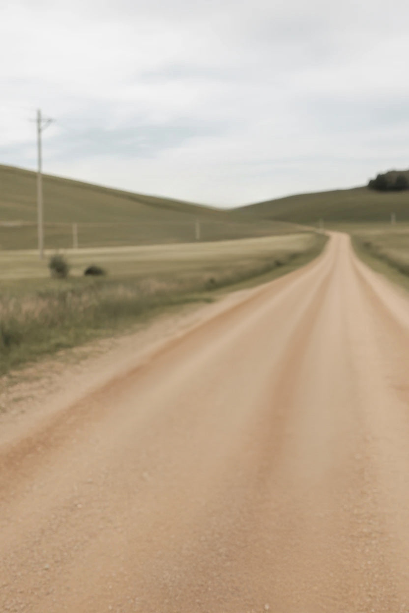 Long winding dirt road through rolling grassy hills