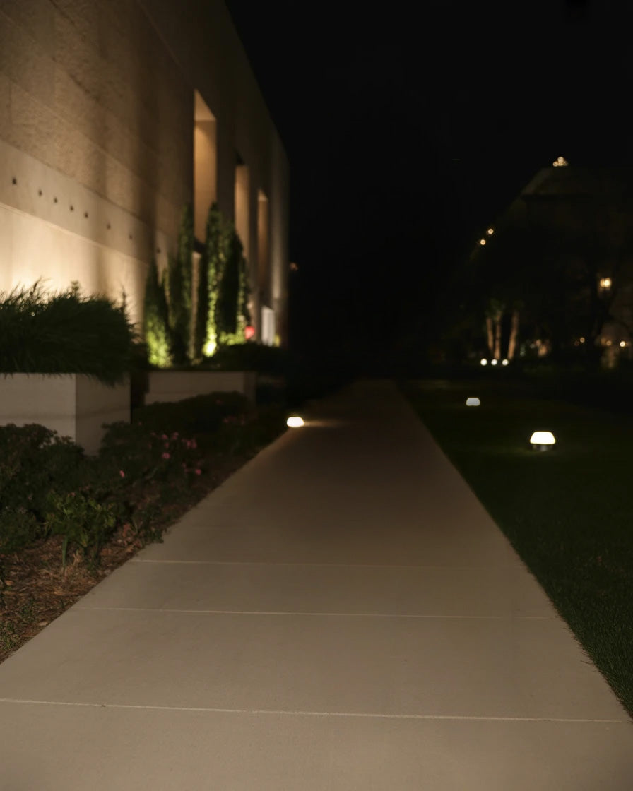 Illuminated garden pathway beside modern building at night