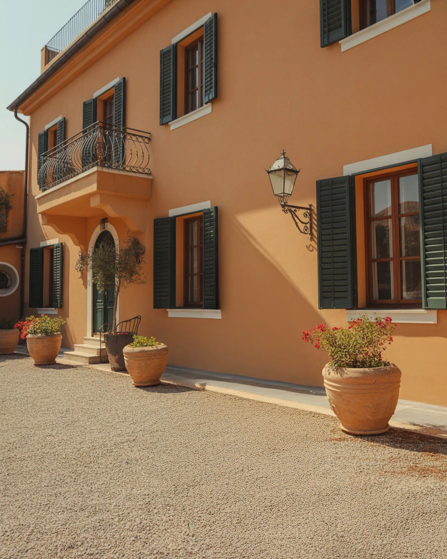 Warm terracotta building facade with green shutters and potted plants