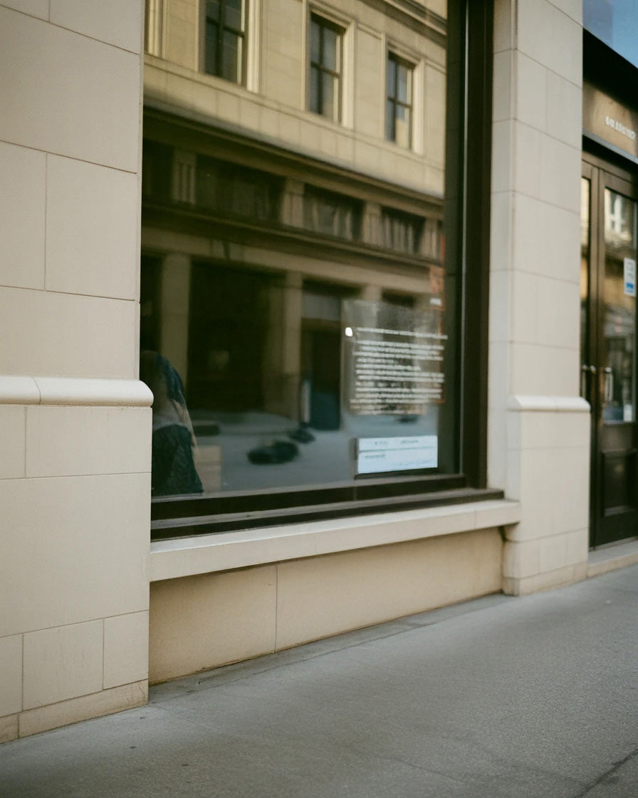 Urban storefront window with building reflections and stone facade