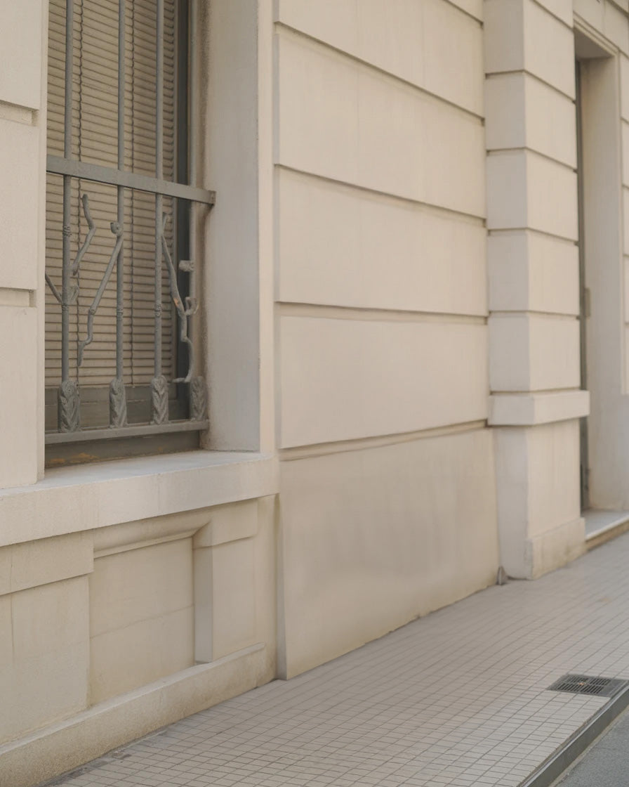 Beige stone building facade with tiled sidewalk and window grill