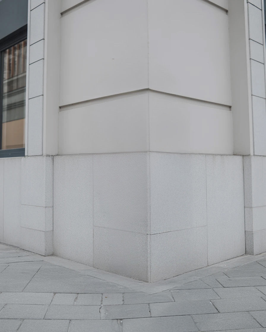 Modern gray stone building corner with tiled pavement base