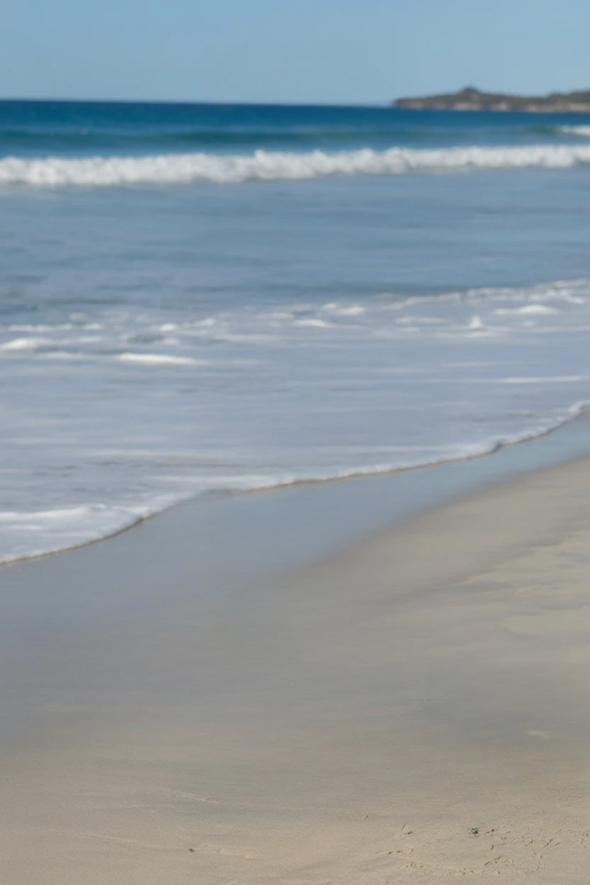 Calm ocean waves washing onto sandy shoreline under blue sky