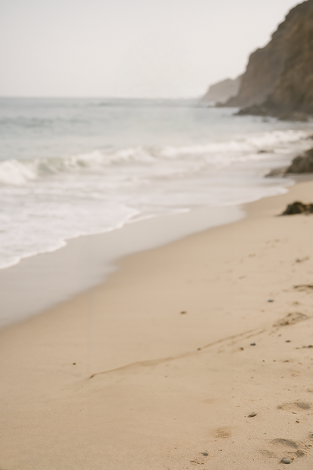 Soft sandy beach with gentle waves and cliffs
