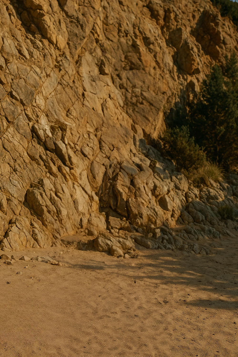 Rocky cliffside with sandy ground and sparse vegetation