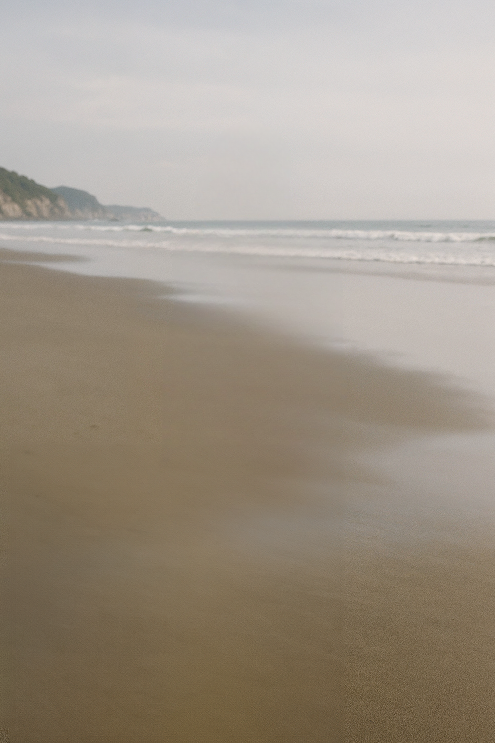 Wide sandy shoreline with gentle waves and distant cliffs