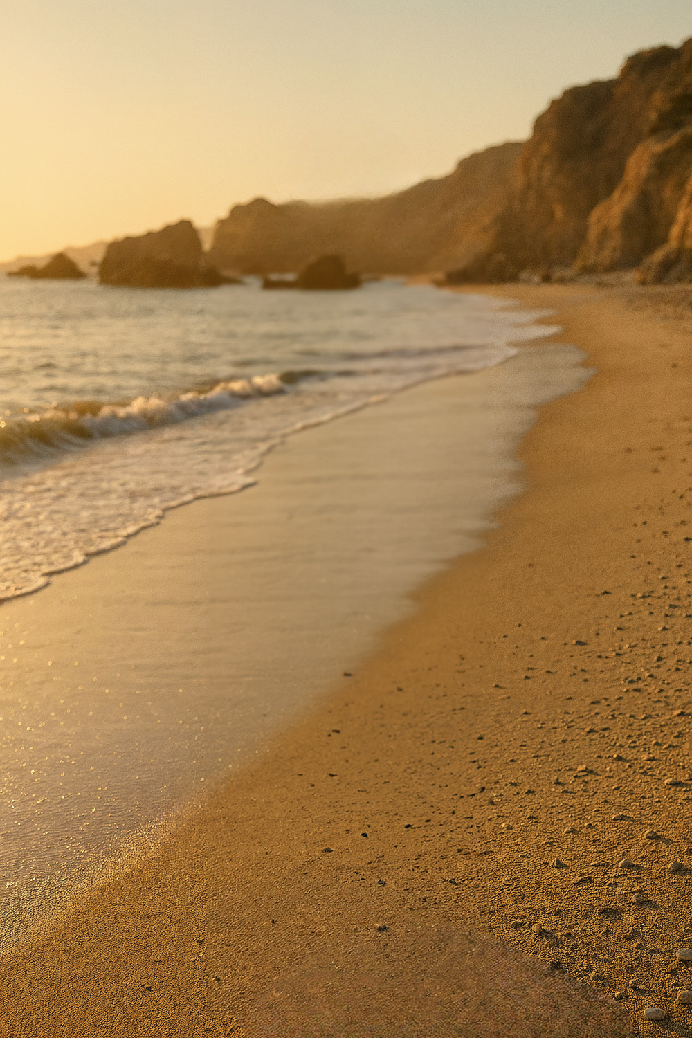 Golden beach shoreline with rocky cliffs at sunset