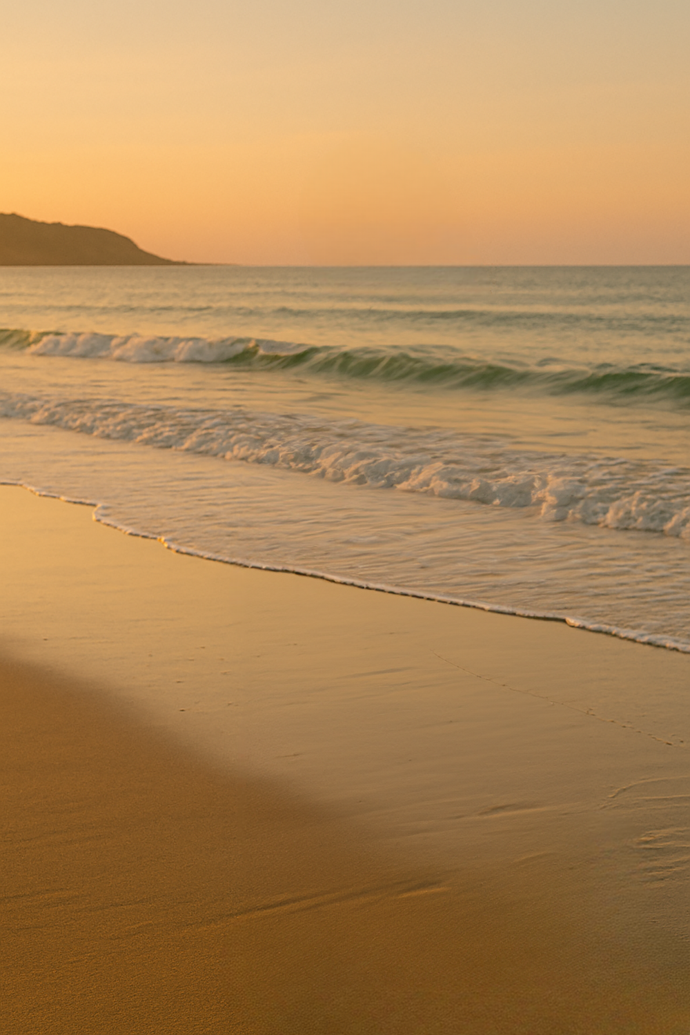 Sunset shoreline with gentle waves and distant headland