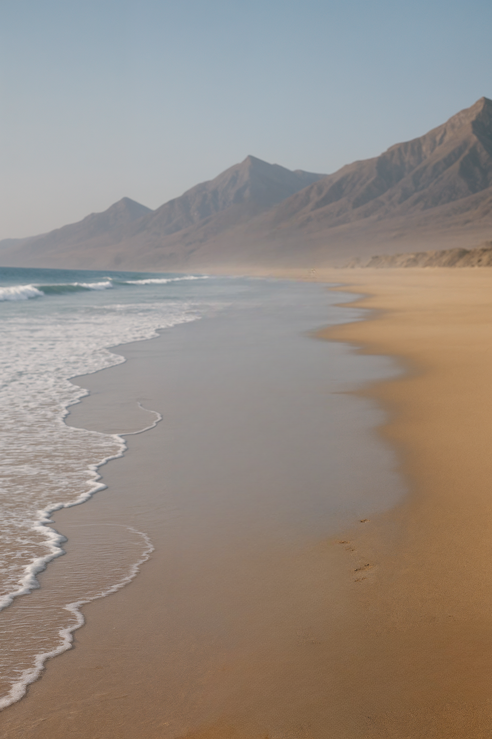 Solitary coastline with mountains rising beyond soft waves