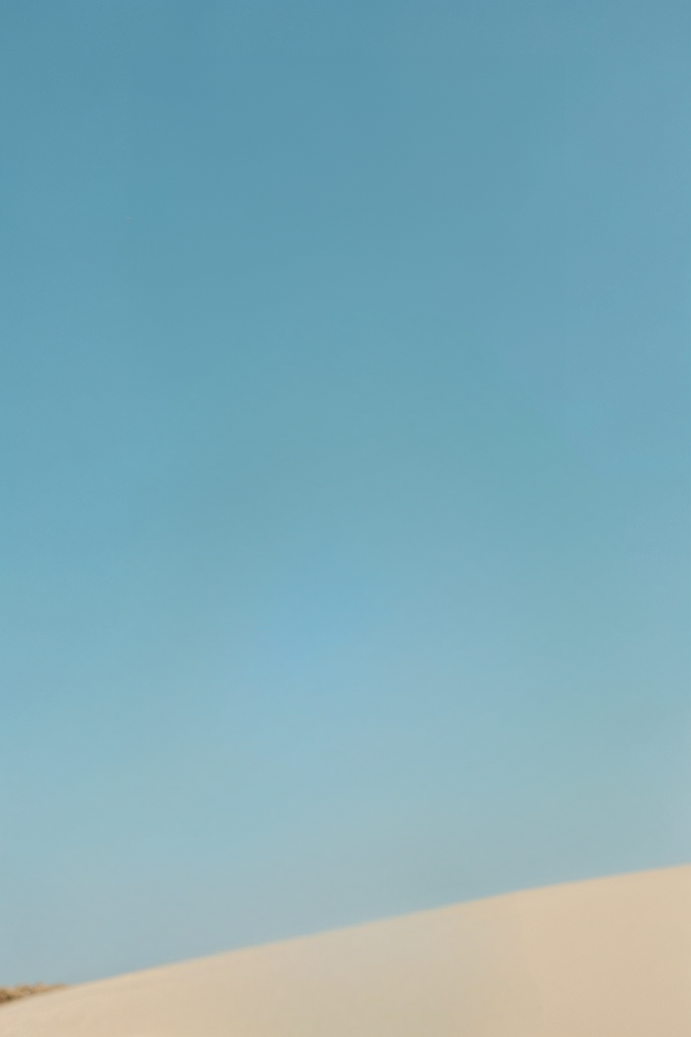 Clear blue sky over smooth, sunlit desert sand dunes