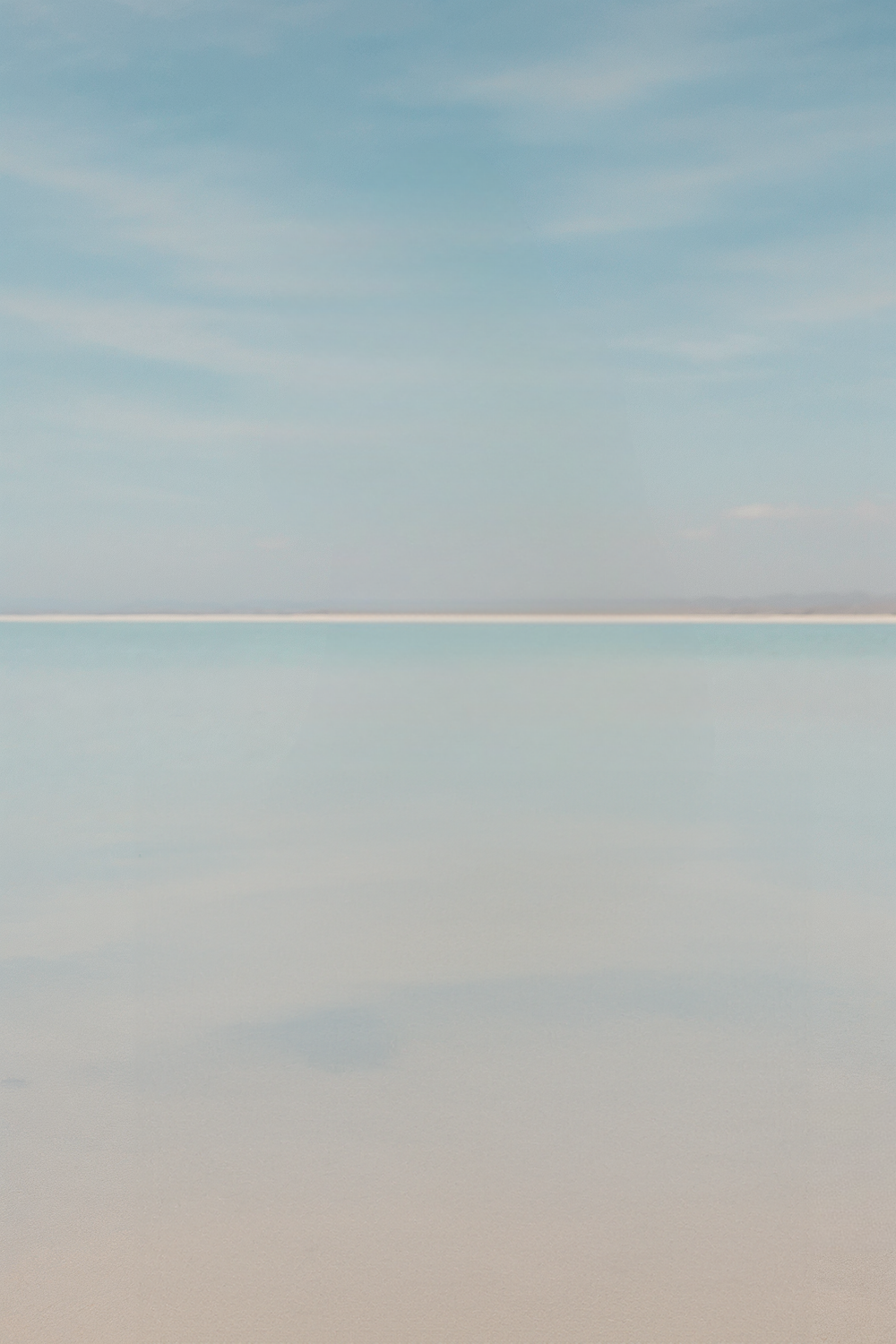 Shallow reflective shoreline under soft blue sky