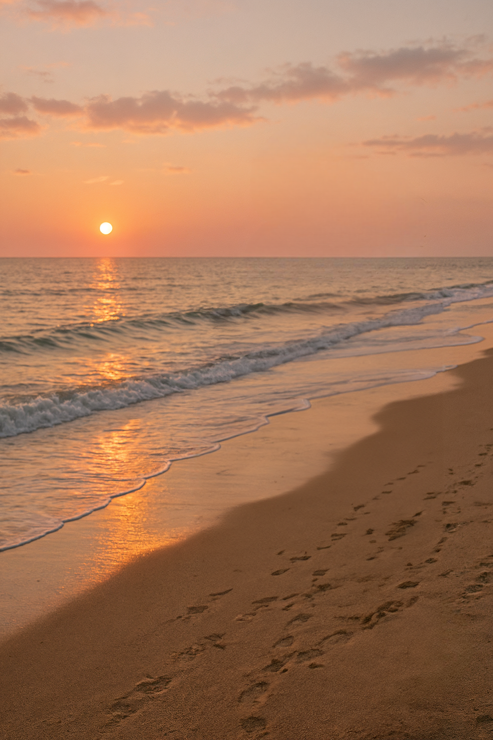 Sunset over calm ocean waves along sandy shoreline