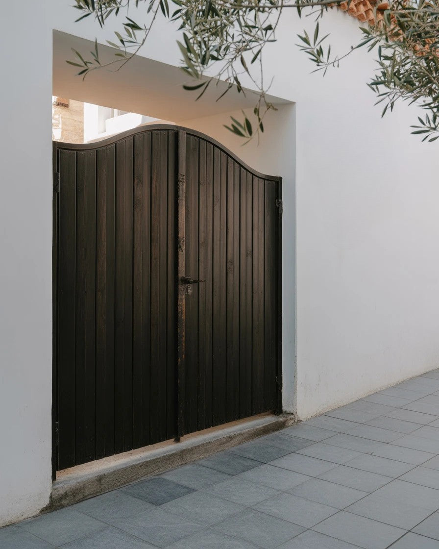 Sunlit wooden gate framed by white stucco walls and tiled walkway