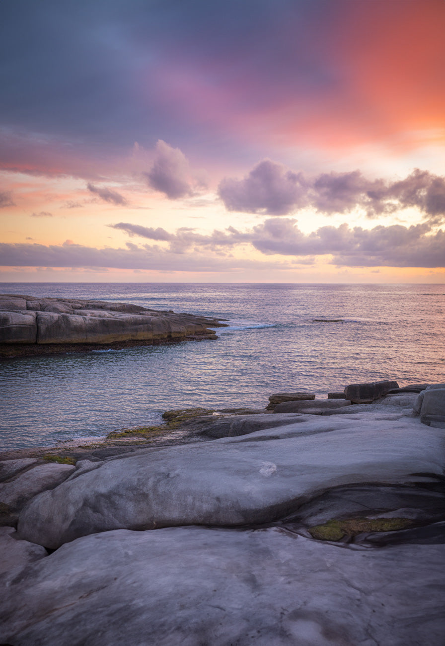 Serene coastal scene with smooth rocky shoreline and calm ocean under a pastel sunset sky