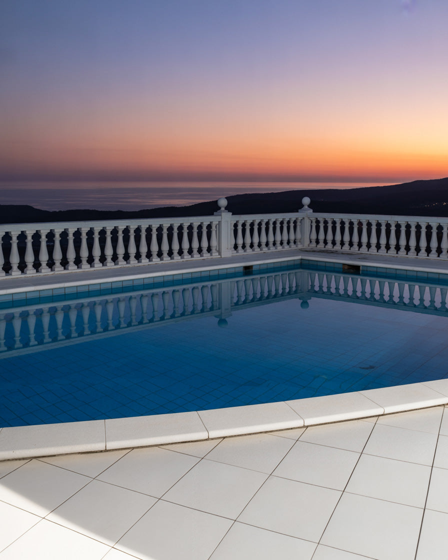Sunset pool overlooking ocean hills with classic white balustrade