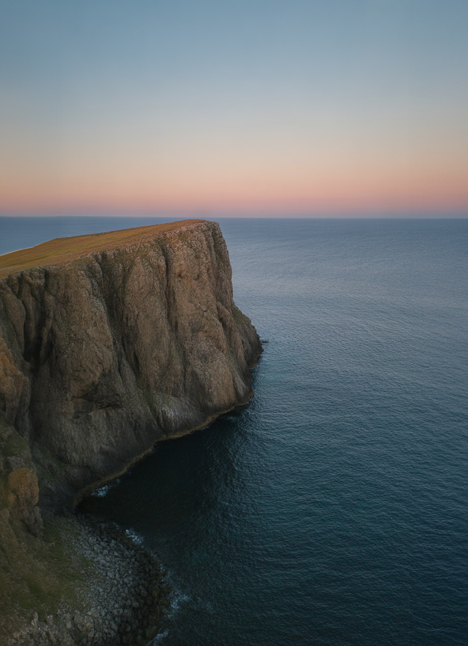 Steep rocky cliff overlooking calm ocean at sunset